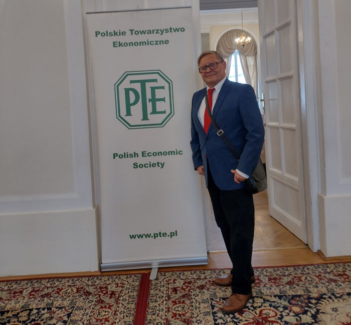 Zdjęcie profesora Marka Szczepańskiego na tle baneru z logo Polskiego Towarzystwa Ekonomocznego