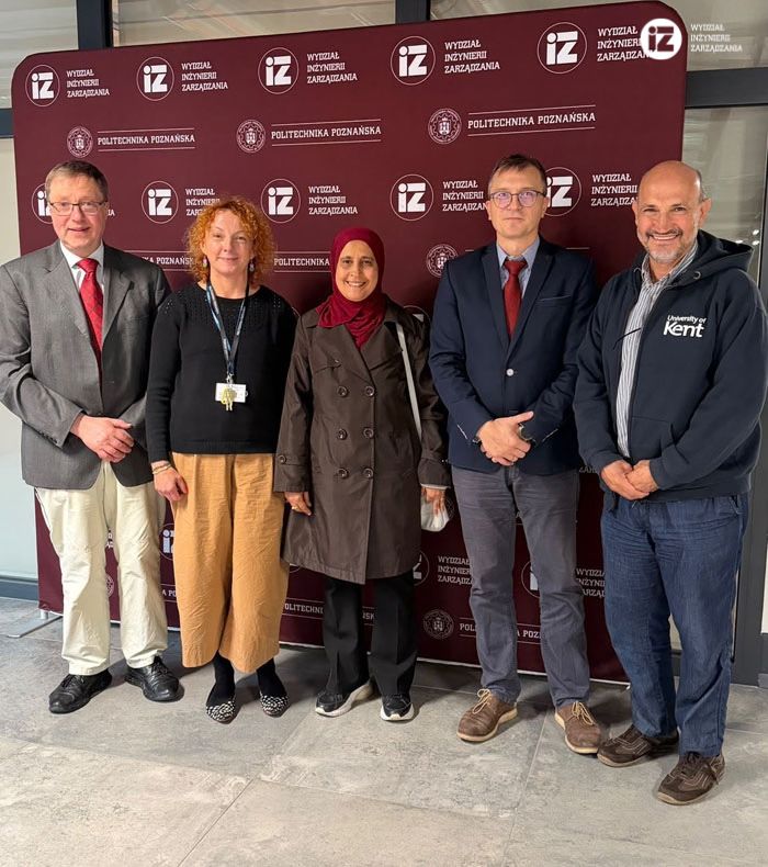 Zdjęcie grupowe na tle ścianki Wydziału Inżynierii Zarządzania. Od lewej prof. Gerhard Wilhelm Weber, dr inż. Joanna Oleśków-Szłapka, żona dr. Chefi Triki, Dziekan dr hab. inż. Marcin Butlewiski i dr Chefi Triki.