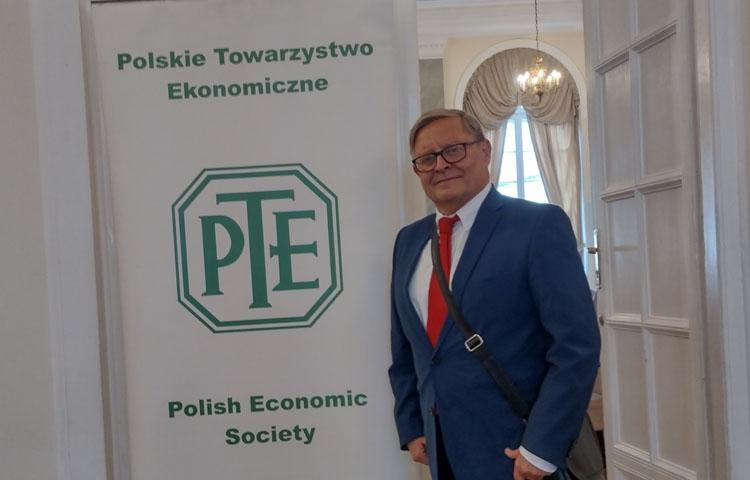 Zdjęcie profesora Marka Szczepańskiego na tle baneru z logo Polskiego Towarzystwa Ekonomocznego