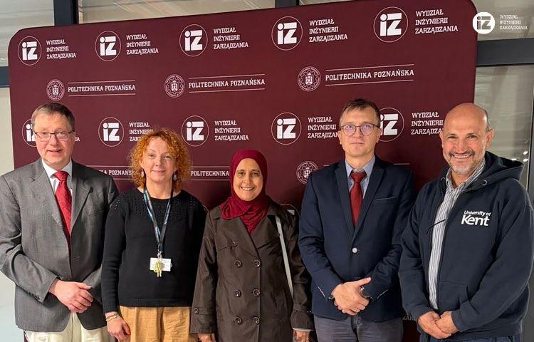 Zdjęcie grupowe na tle ścianki Wydziału Inżynierii Zarządzania. Od lewej prof. Gerhard Wilhelm Weber, dr inż. Joanna Oleśków-Szłapka, żona dr. Chefi Triki, Dziekan dr hab. inż. Marcin Butlewiski i dr Chefi Triki.