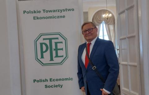 Zdjęcie profesora Marka Szczepańskiego na tle baneru z logo Polskiego Towarzystwa Ekonomocznego