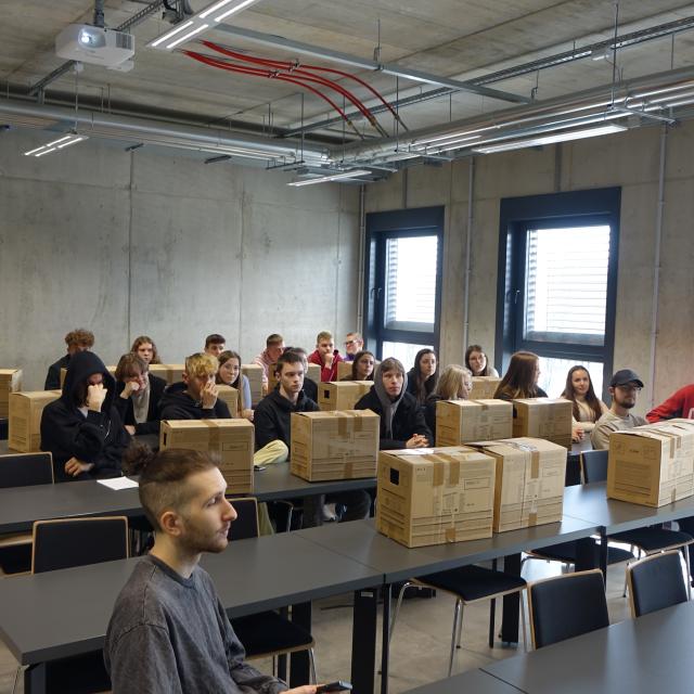 Grupa studentów z pudełkami kartonowymi ustawionymi na ławkach
